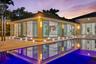 Contemporary exterior featuring floor-to-ceiling sliding glass doors, integrated ground-level accent lighting, stone-tiled patio, and a recessed swimm