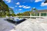 Backyard featuring a custom infinity-edge pool, a raised square spa with tile surfacing, extensive stone paver decking, and a covered pavilion structu