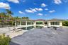 Spacious outdoor living area featuring extensive stone paver hardscaping, an in-ground swimming pool, a covered pavilion, and floor-to-ceiling glass p