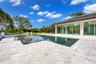 In-ground pool featuring a stone-tile deck, expansive glass sliding doors, and a covered patio area