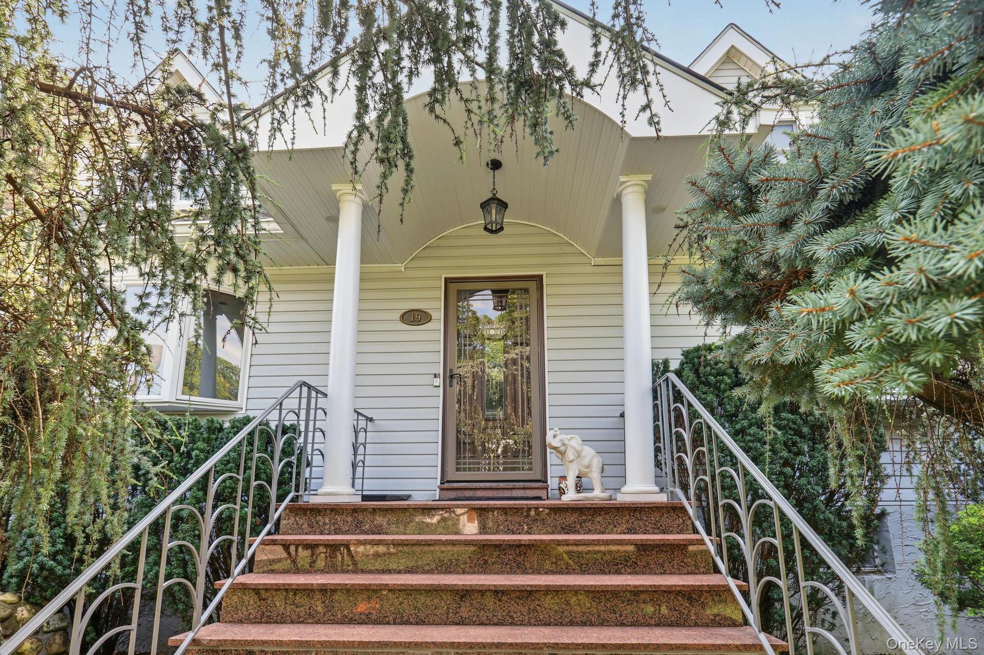 Covered entryway featuring fluted columns, stone-finished steps, decorative metal railings, and a paneled front door