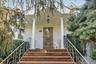 Covered entryway featuring fluted columns, stone-finished steps, decorative metal railings, and a paneled front door