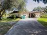 Single-story residence featuring a concrete driveway, attached carport with stone-clad supports, and mature landscaping
