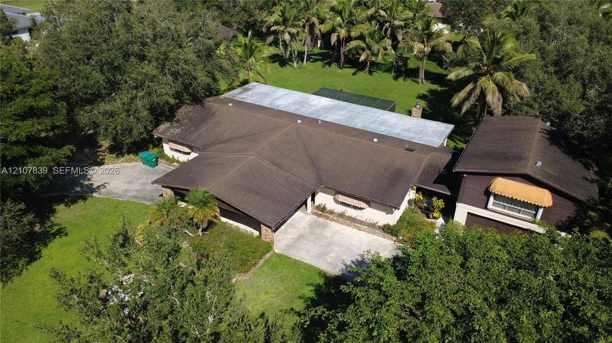 Expansive property featuring a multi-gabled roofline, concrete driveway, attached garage, mature landscaping, and palm trees