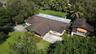 Expansive property featuring a multi-gabled roofline, concrete driveway, attached garage, mature landscaping, and palm trees