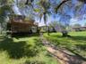 Expansive grounds featuring a natural stone pathway, mature trees, multi-level wood deck, stone-accented exterior, and detached covered parking struct