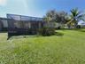 Screened-in enclosure featuring a wood-panel base and lattice siding situated on a spacious grass lawn with mature palm trees
