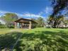 Open-air pavilion featuring stone-clad pillars, a wood-beam ceiling, and an expansive lawn with mature palm trees