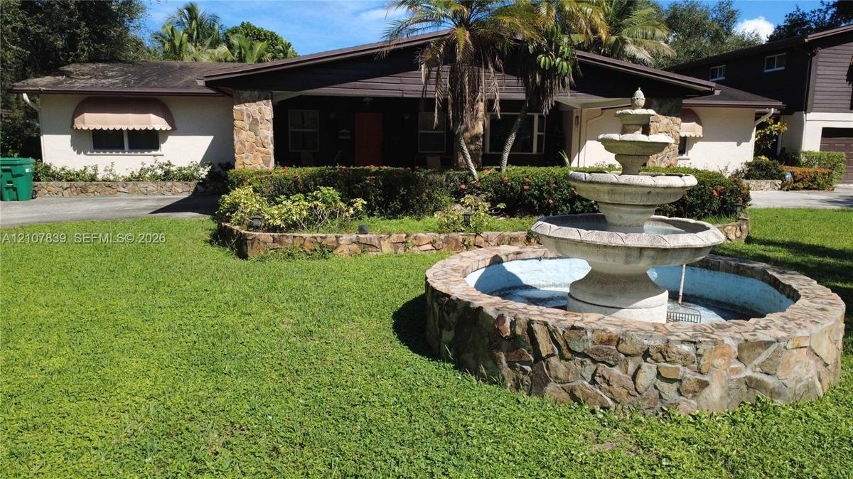 Exterior of the residence featuring natural stone masonry, a tiered stone water fountain, covered entryway, and low-profile roofline