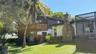 Multi-level exterior featuring a wood-railing deck, exterior stone chimney, screened-in enclosure, and mature palm landscaping