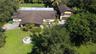 Aerial perspective of a multi-level residence featuring a multi-pitched roof, an attached garage, a stone-lined fountain, and expansive grounds with m
