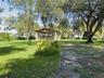 Expansive grounds featuring mature shade trees, a covered pavilion with stone pillars, and gravel landscaping