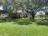 Expansive backyard featuring mature shade trees, a manicured lawn, a detached covered structure, and a raised wooden deck