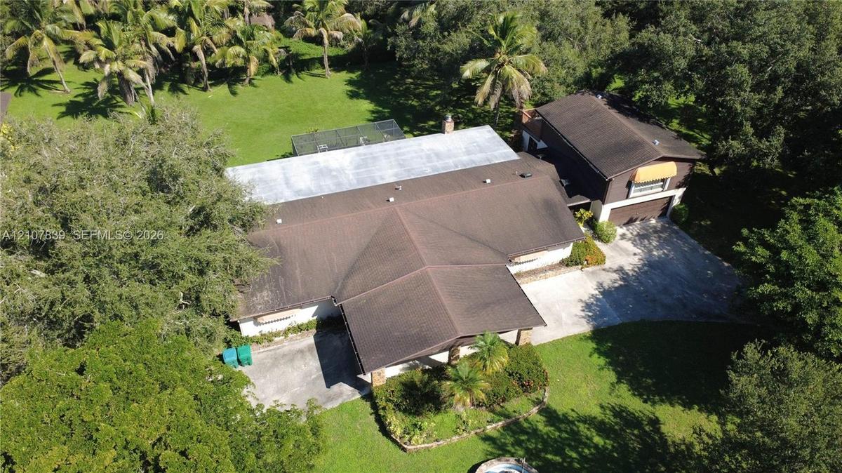Aerial perspective of a multi-level residence featuring a multi-pitched roof, paved driveway, mature trees, and an expansive lawn