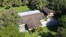 Aerial perspective of a multi-level residence featuring a multi-pitched roof, paved driveway, mature trees, and an expansive lawn