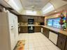 Kitchen featuring wood cabinetry, a coffered ceiling with integrated lighting, a ceiling fan, tiled flooring, and a window above a dual-basin sink