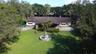Single-story residence featuring a covered portico, stone-accented facade, central tiered water fountain, and expansive lawn surrounded by mature tree