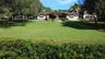 Expansive front lawn with a stone-clad central fountain, mature trees, manicured hedges, and an attached multi-car garage