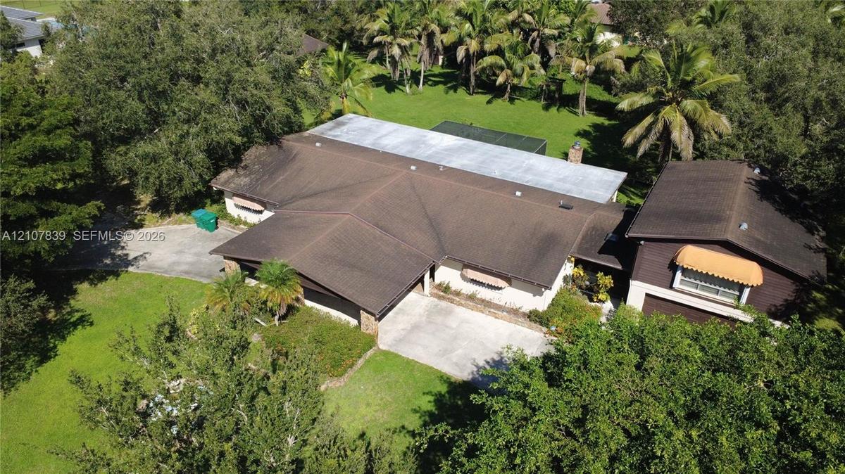 Aerial view of property featuring a multi-section roofline, concrete driveway, expansive lawn, and mature palm and shade trees
