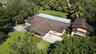 Aerial view of property featuring a multi-section roofline, concrete driveway, expansive lawn, and mature palm and shade trees