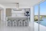 Modern kitchen featuring a waterfall-edge island, high-gloss cabinetry, integrated stainless steel appliances, polished stone-finish flooring, and flo