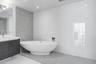 Freestanding oval soaking tub, wall-mounted faucet, custom dark wood-finish vanity with integrated sink, grey textured tile accent wall, and polished 