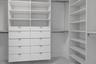 Custom closet system featuring white built-in cabinetry, adjustable open shelving, integrated drawers with metallic pulls, and hanging rods