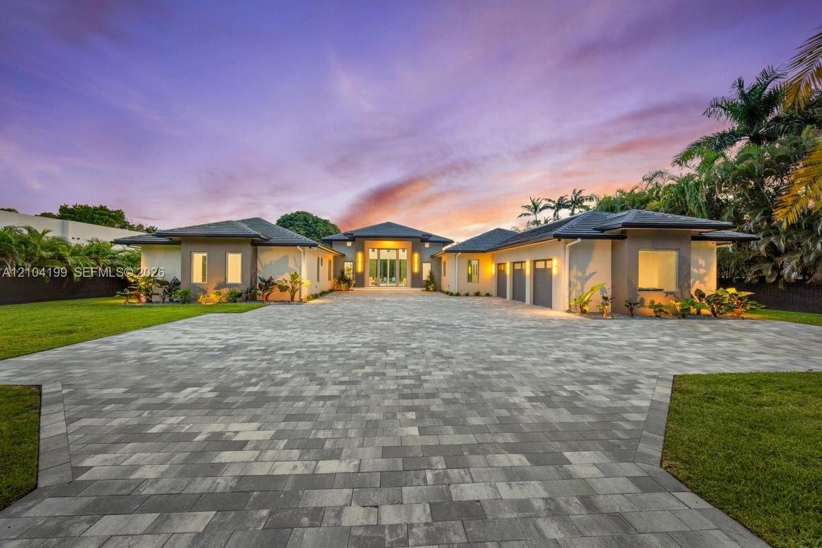Single-story residence featuring a multi-car garage, expansive paver driveway, hip roof architecture, and landscaped grounds