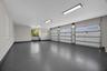 Three-car garage featuring a speckled epoxy-coated floor, bright LED panel lighting, and three sectional garage doors with frosted windows
