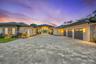 Contemporary exterior featuring a paved stone driveway, three-car garage, recessed entryway with floor-to-ceiling glass, and low-profile tile roofing