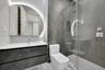 Bathroom featuring a floating vanity with a white countertop, an arched LED-backlit mirror, large-format grey tile walling, and a walk-in shower with 
