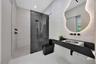 Bathroom featuring a wall-mounted floating vanity with a stone countertop, backlit organic-shaped mirror, matte black fixtures, and a walk-in shower w