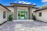 Modern architectural exterior featuring a paved stone driveway, recessed entry with a double-height frame, full-height glass entryway, and vertical wa