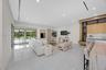 Open-concept living space featuring large-format tile flooring, recessed linear lighting, sliding glass walls, and custom cabinetry with stone-surface