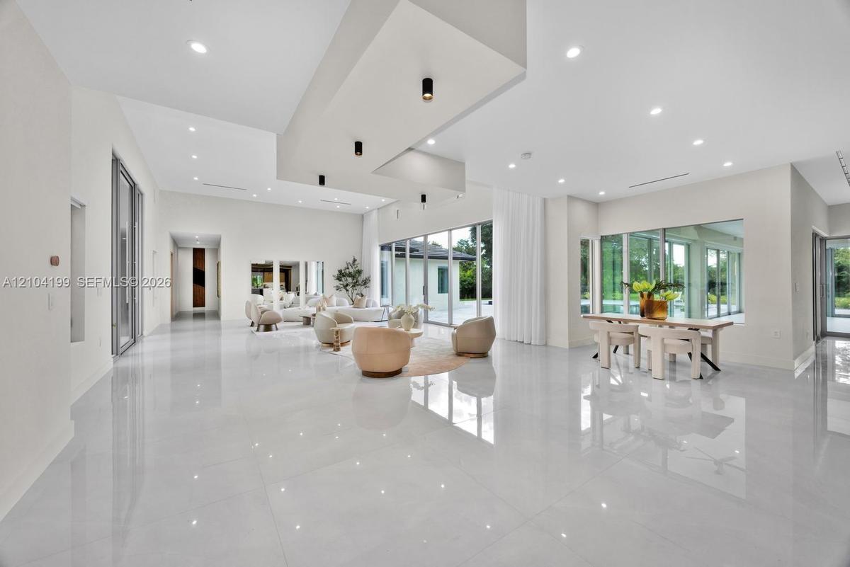 Open-concept living space featuring high-gloss tile flooring, recessed lighting, a tiered tray ceiling with cylindrical pendant fixtures, and floor-to