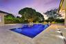 In-ground swimming pool with built-in spa, stone paver patio, and mature tree landscaping