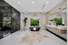 Full-wall stone slab surrounds, floating wood-finish dual vanity with integrated countertop, dark soaking tub, recessed ceiling lighting, and polished