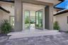 Modern entryway featuring an oversized glass pivot door, dual tiered concrete steps, linear wall-mounted exterior lighting, and a paved stone driveway