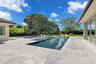 Outdoor living area featuring stone paver decking, an in-ground infinity-edge pool, a raised spa, and floor-to-ceiling glass sliding doors