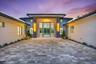 Modern stucco exterior featuring a tiered roofline, expansive paver courtyard, floor-to-ceiling glass entryway, and wall-mounted linear lighting