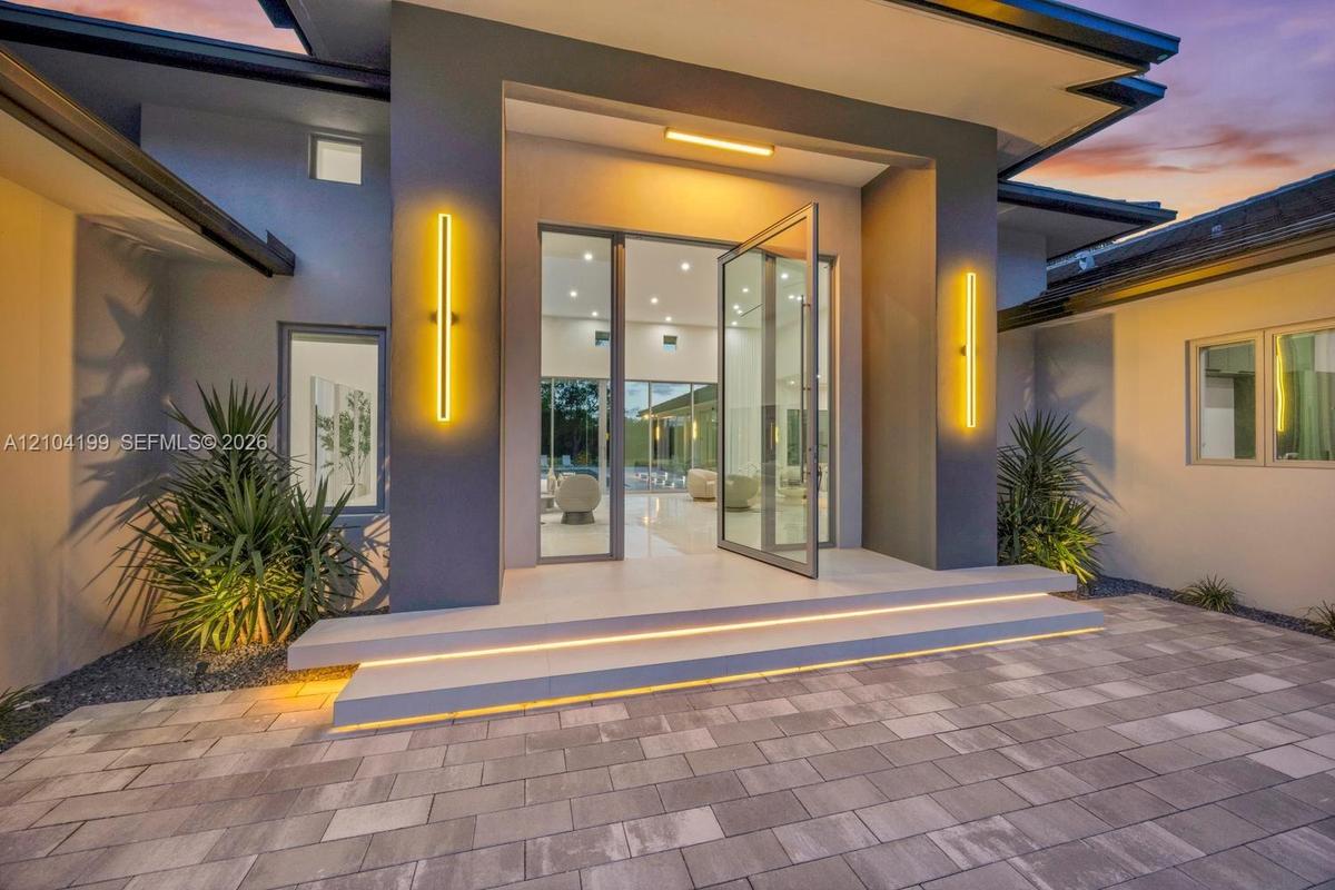 Modern exterior entrance featuring a glass-panel pivoting entry door, dual elevated concrete steps with integrated lighting, sleek vertical wall sconc