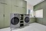 Full-height sage green cabinetry with matte black hardware, stone-surface backsplash, integrated shelving, and white tile flooring