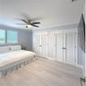 Wood-finish flooring, dual sets of louvered closet doors with matte black hardware, and a ceiling-mounted light fixture with integrated fan blades