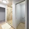 Walk-in shower with frameless glass enclosure, stone-tile surround, built-in shelving, and adjustable handheld shower head, complemented by stone-tile