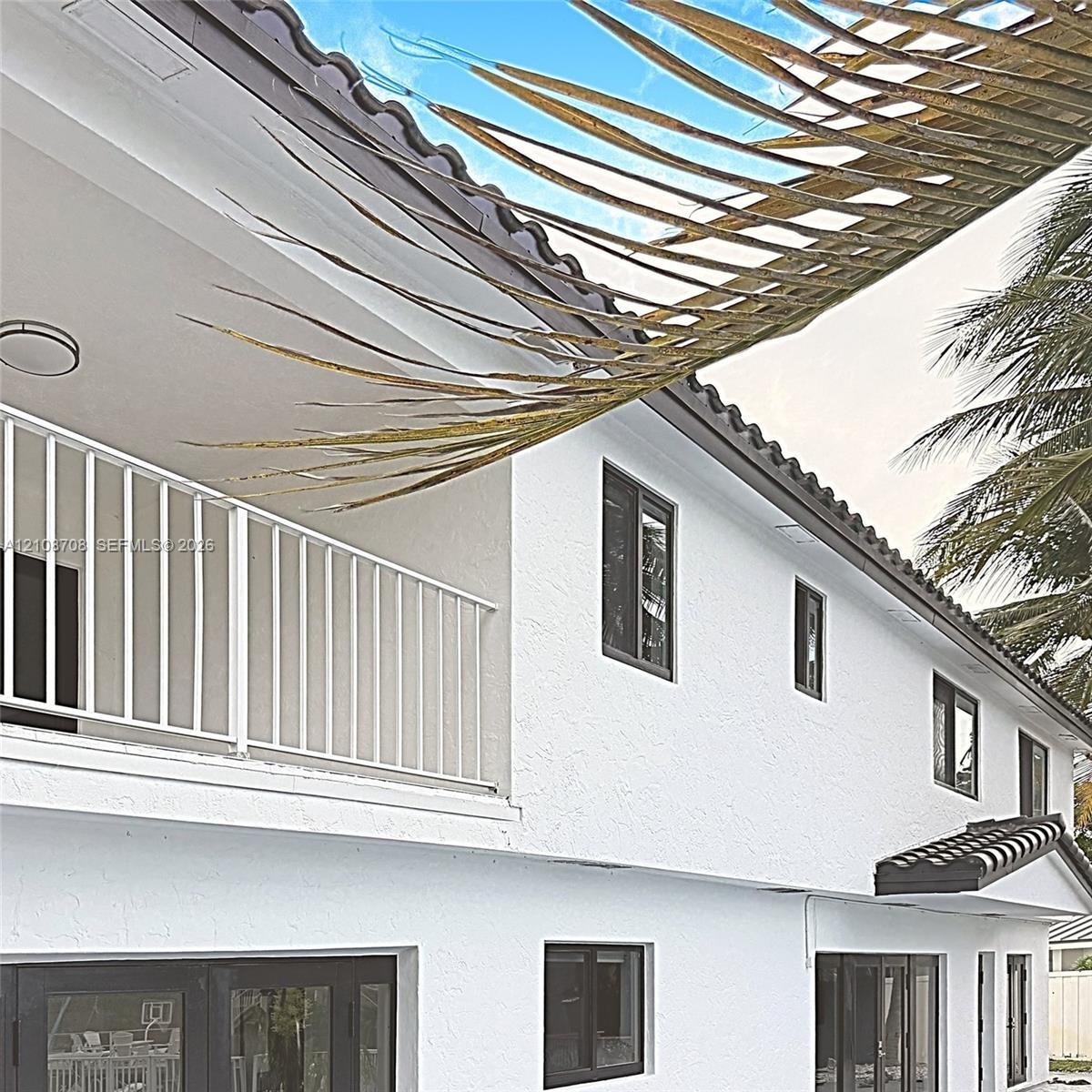 Exterior elevation featuring a stucco facade, dark-frame windows, a tiled roofline, and a covered balcony with a white metal railing