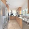 Kitchen featuring natural wood cabinetry, stone-finish countertops, stainless steel appliances, a center island with a chimney-style range hood, and t