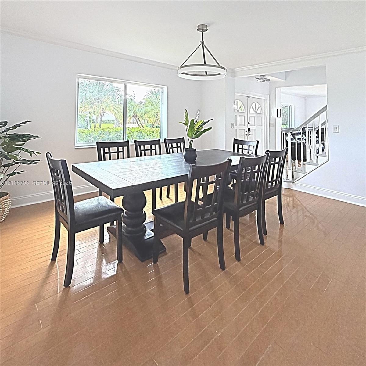 Wood-finish flooring, crown molding, a modern multi-tier chandelier, and a large window featuring outdoor scenery