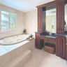 Jetted soaking tub with a tiled surround, custom wood-finish cabinetry, dark stone countertop, and full-wall natural stone tile surfacing