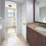 Dark wood vanity featuring a stone countertop, integrated sink, large-format tile flooring, and a glass-enclosed shower