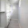 Walk-in closet featuring custom white built-in shelving, integrated three-drawer storage, adjustable garment rods, wood-finish flooring, and a small h